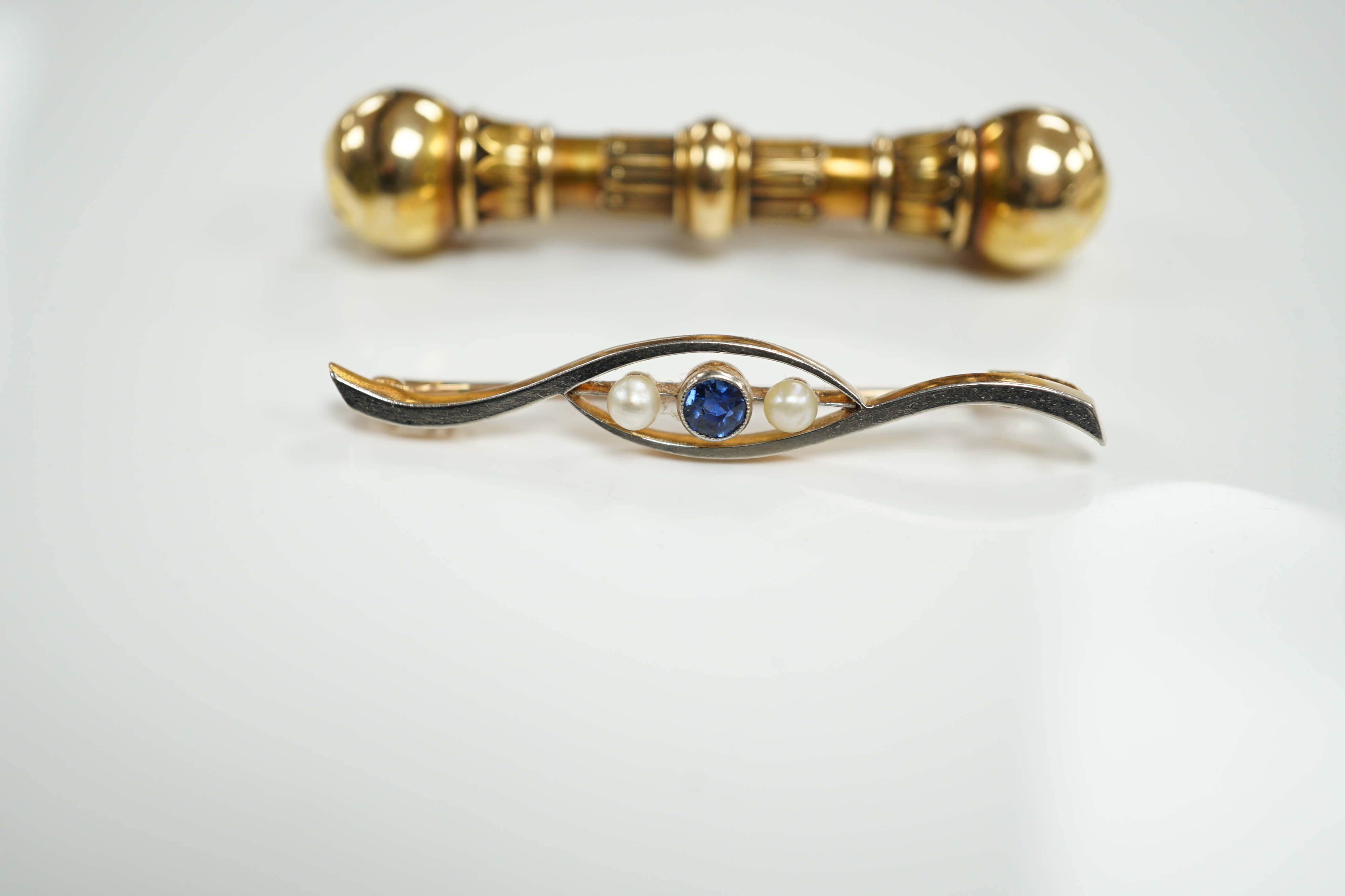 A Victorian yellow metal 'dumbbell' bar brooch, with engraved inscription dated 1862, 56mm and a later 15ct, sapphire and seed pearl set three stone crossover bar brooch.